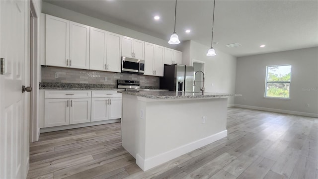 kitchen featuring appliances with stainless steel finishes, white cabinets, and an island with sink