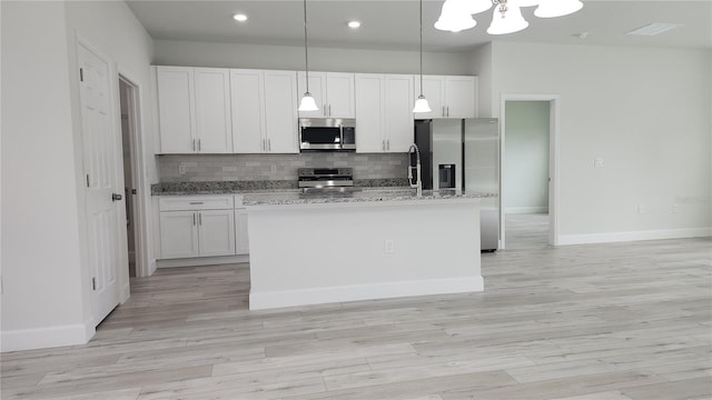 kitchen with appliances with stainless steel finishes, white cabinets, a kitchen island with sink, and decorative light fixtures