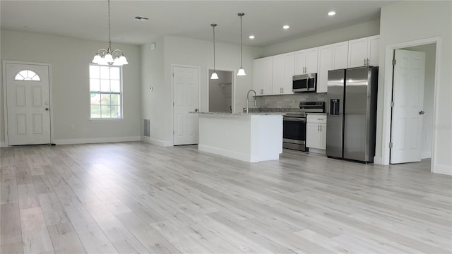 kitchen with appliances with stainless steel finishes, white cabinets, decorative light fixtures, and an island with sink