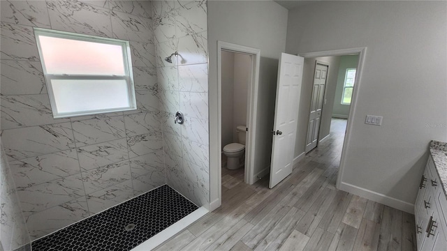 bathroom with a tile shower, hardwood / wood-style flooring, toilet, and plenty of natural light