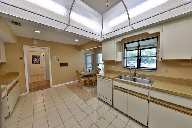 kitchen featuring white dishwasher, sink, light tile patterned floors, and white cabinets