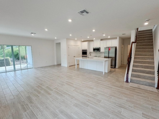 kitchen with light hardwood / wood-style floors, a kitchen island with sink, sink, stainless steel appliances, and white cabinetry