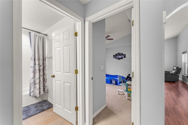 bathroom featuring hardwood / wood-style floors, ceiling fan, shower / bath combination with curtain, and a textured ceiling