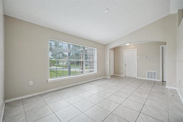 spare room with light tile patterned flooring, vaulted ceiling, and a textured ceiling