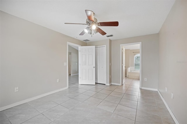 unfurnished bedroom featuring light tile patterned flooring, ensuite bathroom, ceiling fan, and a closet