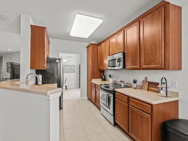 kitchen featuring sink, light tile patterned floors, kitchen peninsula, a textured ceiling, and appliances with stainless steel finishes