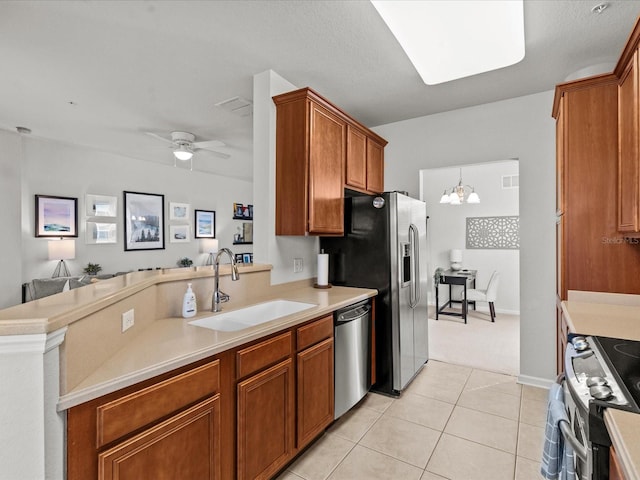 kitchen with light tile patterned flooring, sink, kitchen peninsula, stainless steel appliances, and ceiling fan with notable chandelier