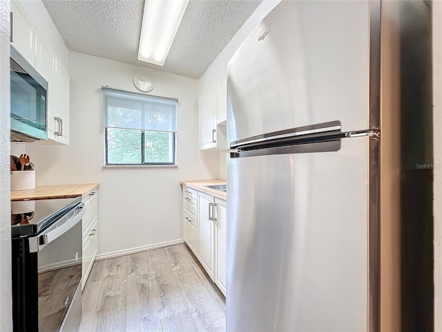 kitchen featuring white cabinetry, light hardwood / wood-style floors, stainless steel appliances, and a textured ceiling