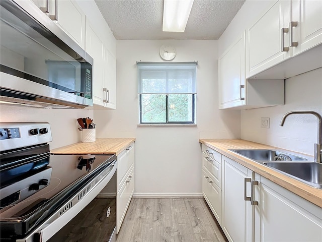 kitchen featuring white cabinetry, wood counters, light hardwood / wood-style flooring, sink, and stainless steel appliances