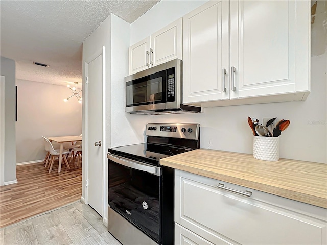 kitchen featuring a textured ceiling, appliances with stainless steel finishes, light hardwood / wood-style flooring, and white cabinets