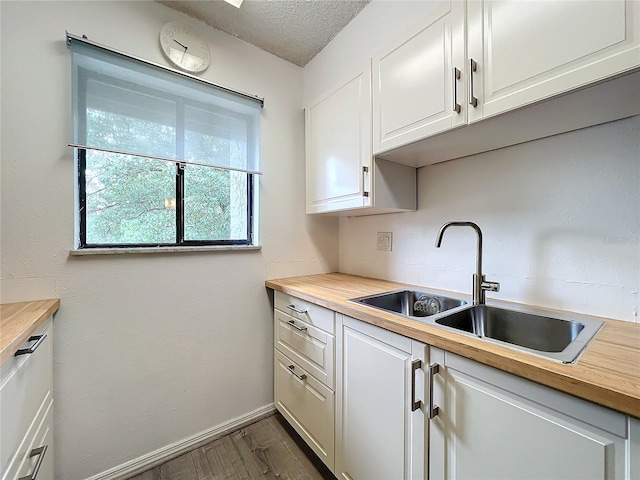 kitchen featuring sink, butcher block counters, a textured ceiling, white cabinets, and dark wood-type flooring