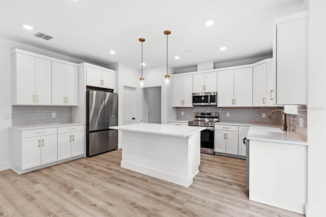 kitchen featuring a kitchen island, appliances with stainless steel finishes, light wood-type flooring, sink, and decorative light fixtures