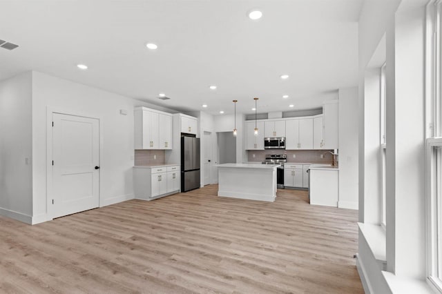 kitchen featuring white cabinets, hanging light fixtures, a kitchen island, light hardwood / wood-style floors, and stainless steel appliances