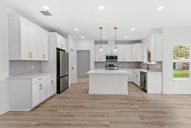 kitchen featuring appliances with stainless steel finishes, white cabinets, a center island, and hanging light fixtures