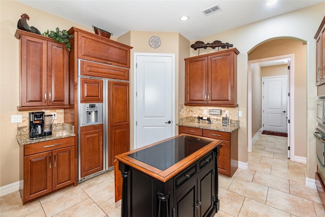 kitchen with light stone counters, a kitchen island, black electric cooktop, paneled fridge, and decorative backsplash