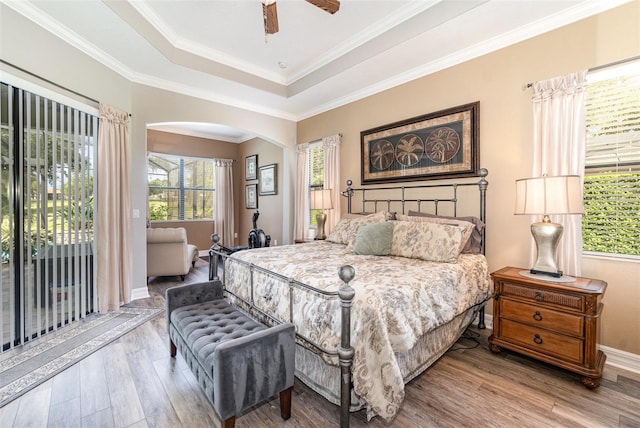 bedroom with ceiling fan, wood-type flooring, a raised ceiling, crown molding, and access to outside