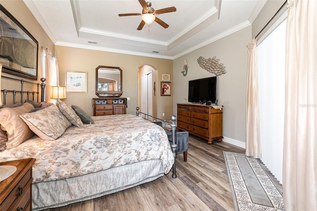 bedroom with a raised ceiling, wood-type flooring, ornamental molding, and ceiling fan