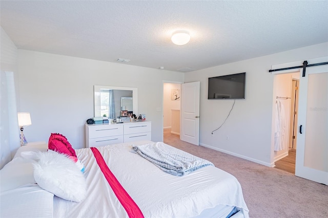 bedroom featuring a barn door, a textured ceiling, and light carpet