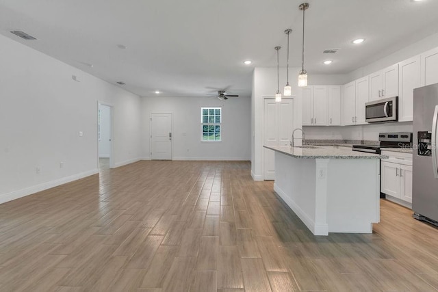 kitchen with stainless steel appliances, a center island with sink, light wood-type flooring, white cabinetry, and light stone counters