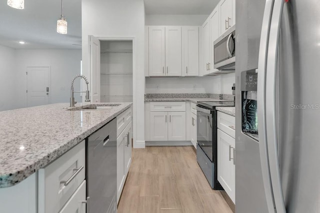 kitchen with light stone countertops, appliances with stainless steel finishes, sink, hanging light fixtures, and white cabinetry