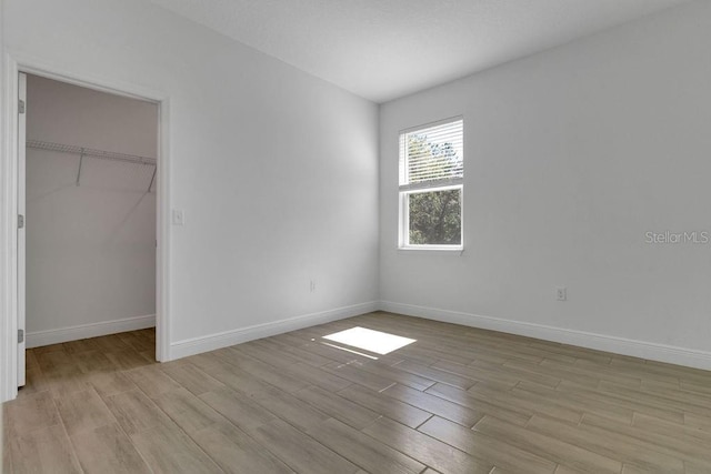 unfurnished bedroom featuring a closet, a walk in closet, and light hardwood / wood-style floors