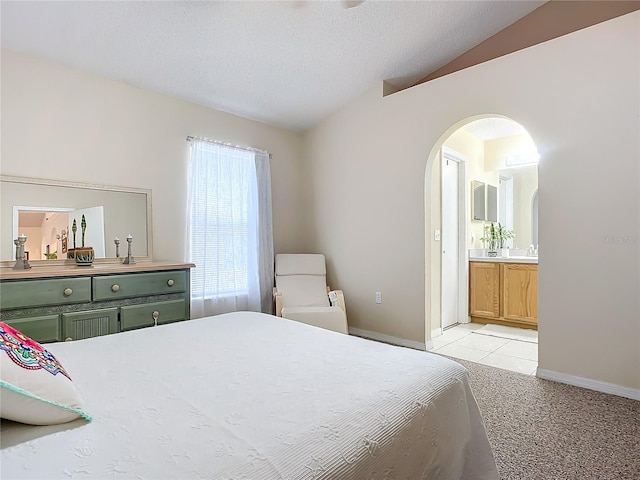 bedroom with light carpet, a textured ceiling, ensuite bath, and vaulted ceiling