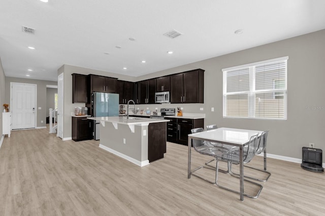 kitchen featuring dark brown cabinets, an island with sink, light hardwood / wood-style flooring, sink, and stainless steel appliances