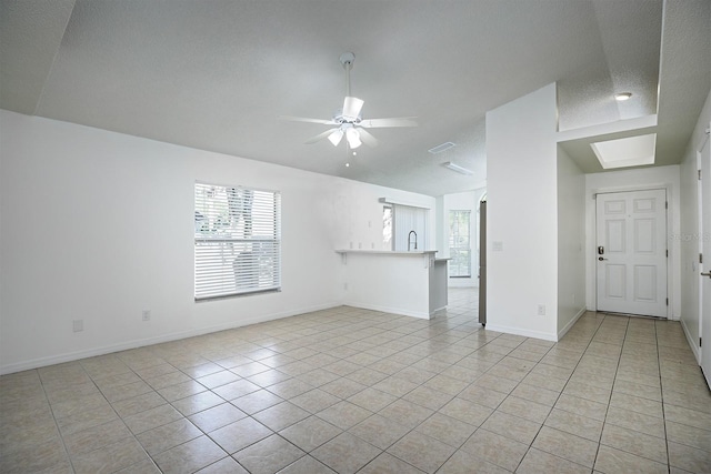 unfurnished living room with a skylight, ceiling fan, light tile patterned floors, and a textured ceiling