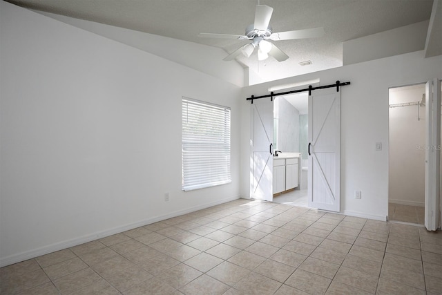 tiled empty room featuring ceiling fan, a textured ceiling, lofted ceiling, and a barn door