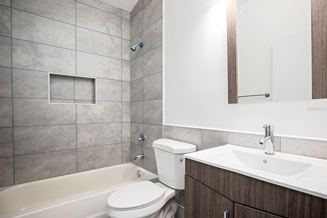 full bathroom with tile walls, tiled shower / bath, vanity, and toilet