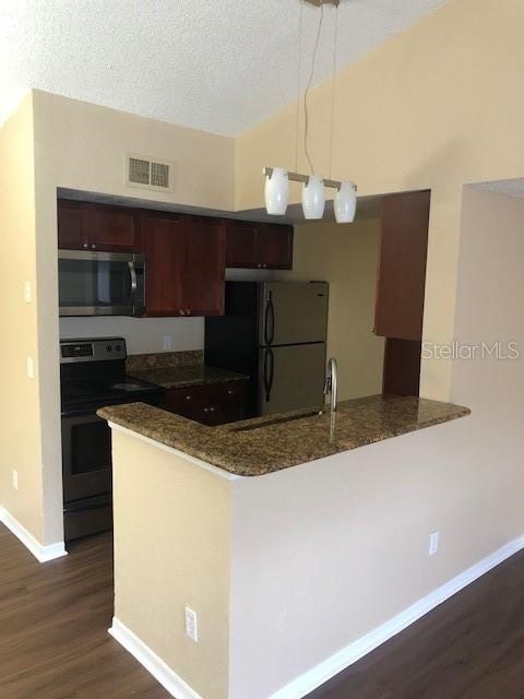 kitchen featuring kitchen peninsula, hanging light fixtures, stainless steel appliances, a textured ceiling, and dark hardwood / wood-style flooring