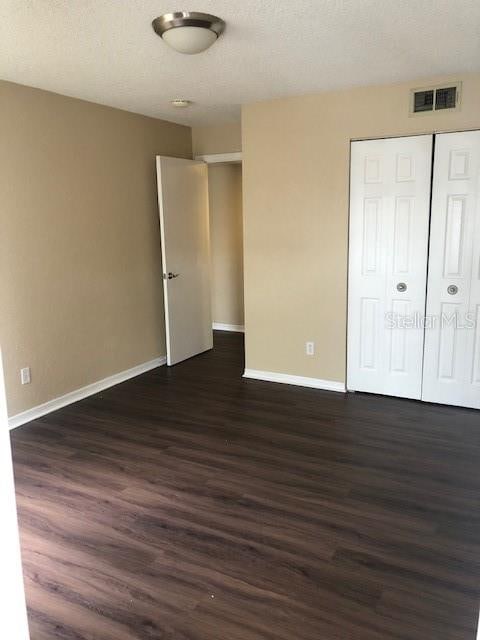 unfurnished bedroom with a closet, a textured ceiling, and dark hardwood / wood-style flooring