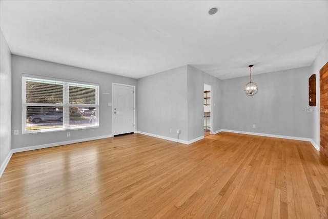 unfurnished living room featuring an inviting chandelier and light hardwood / wood-style flooring