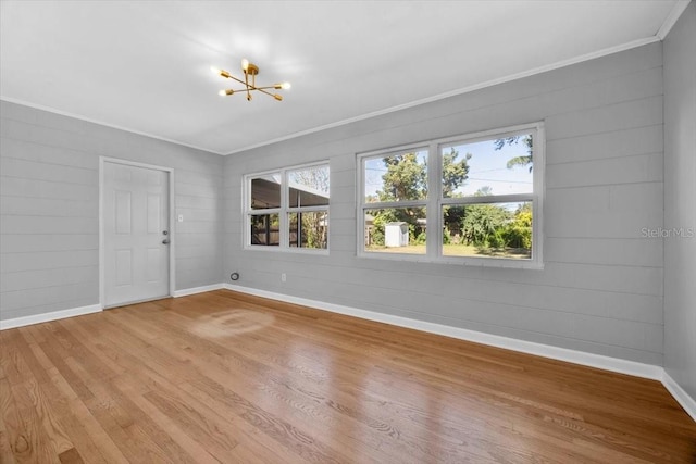 spare room with hardwood / wood-style flooring, an inviting chandelier, plenty of natural light, and ornamental molding