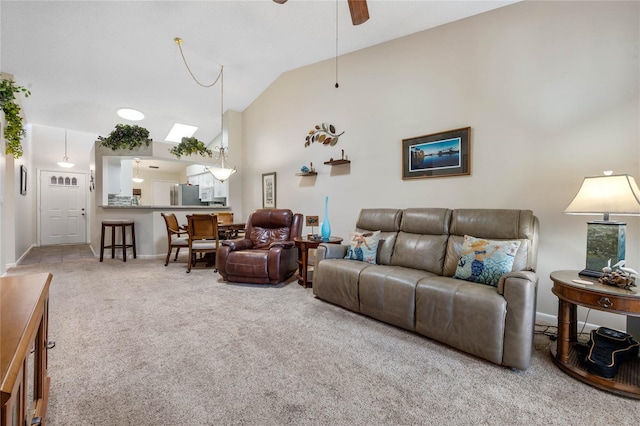 carpeted living room with ceiling fan and vaulted ceiling with skylight