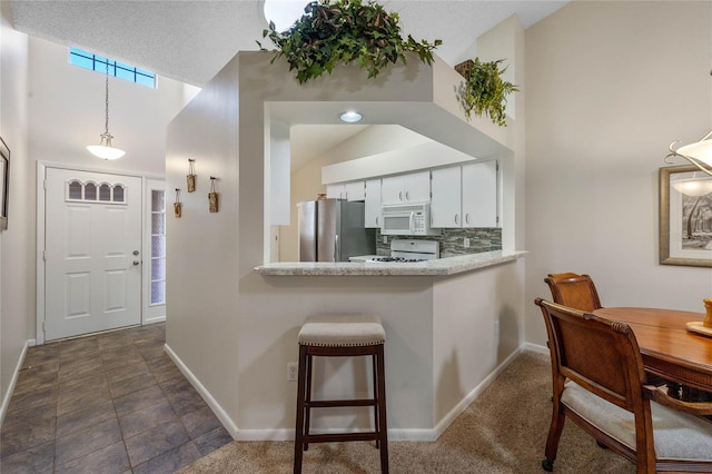 kitchen with white appliances, decorative light fixtures, lofted ceiling, white cabinets, and a textured ceiling