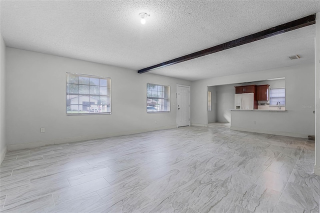 unfurnished living room featuring beamed ceiling and a textured ceiling