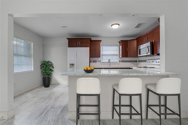 kitchen with light stone countertops, kitchen peninsula, tasteful backsplash, and white appliances