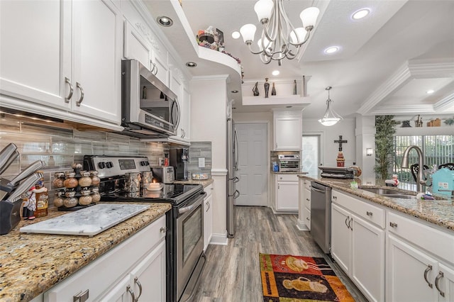 kitchen with ornamental molding, stainless steel appliances, sink, white cabinets, and hanging light fixtures