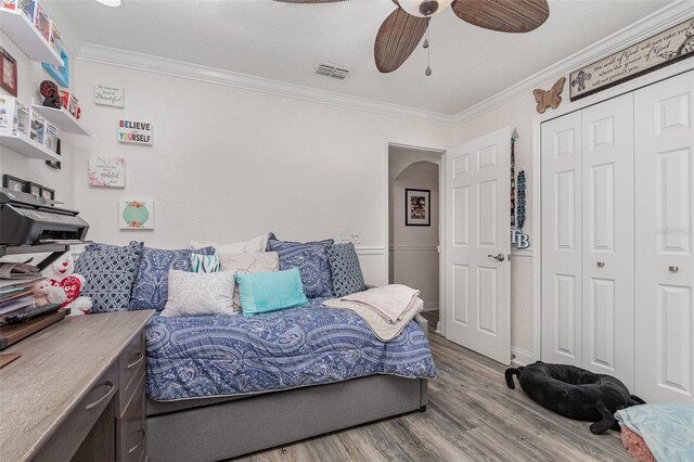 bedroom featuring wood-type flooring, a closet, ceiling fan, and ornamental molding