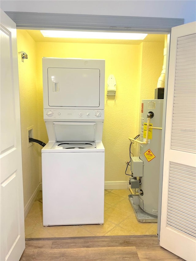 washroom featuring stacked washer / dryer, water heater, and light hardwood / wood-style flooring