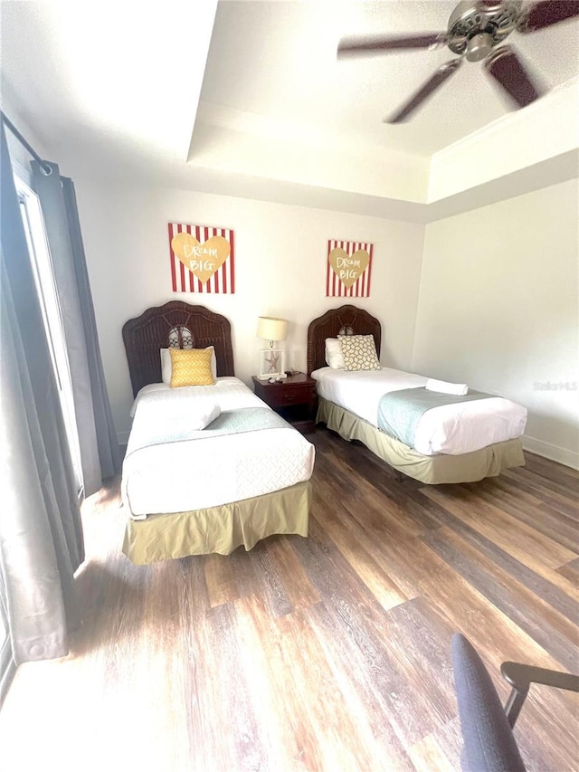 bedroom with ceiling fan, a tray ceiling, and wood-type flooring