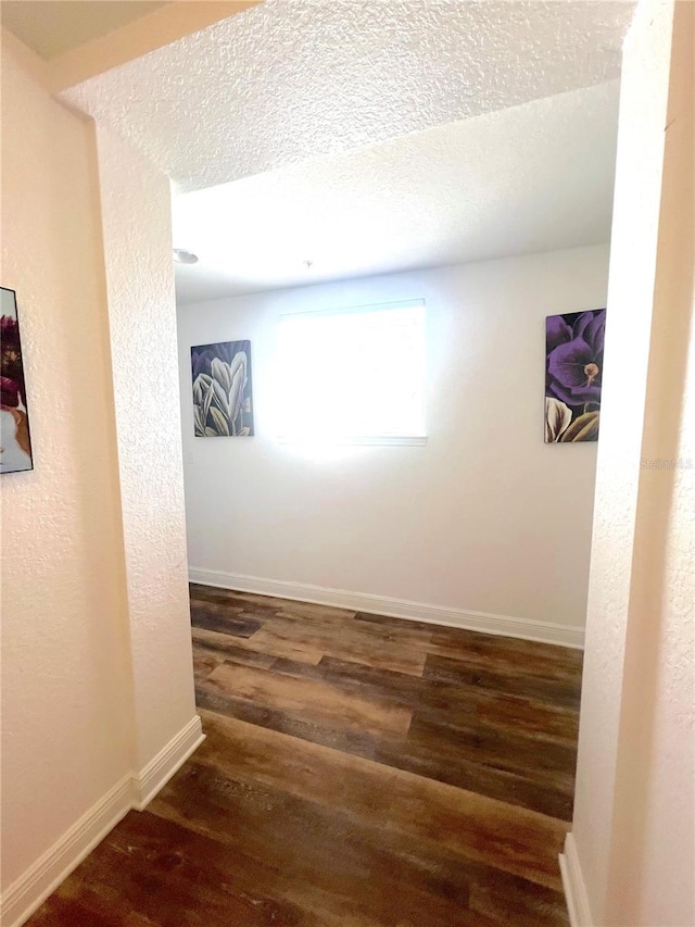 corridor with a textured ceiling and dark hardwood / wood-style floors