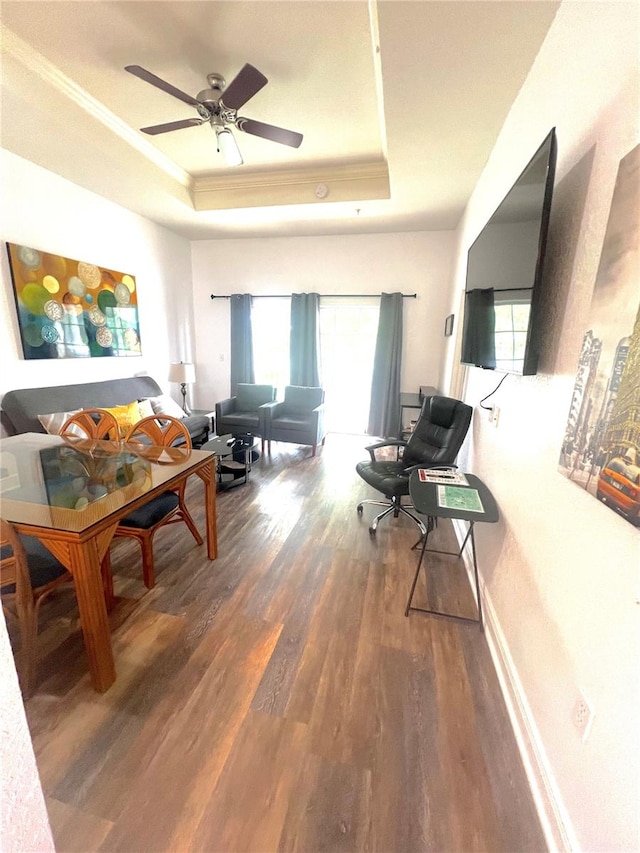 living room with a raised ceiling, wood-type flooring, ornamental molding, and ceiling fan