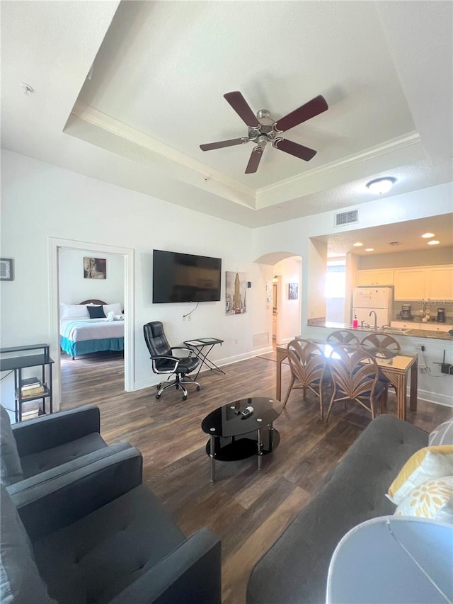 living room with wood-type flooring, a raised ceiling, crown molding, and ceiling fan