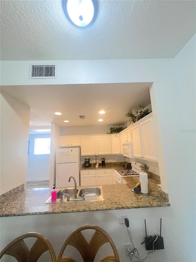 kitchen with white appliances, sink, kitchen peninsula, white cabinetry, and a kitchen bar