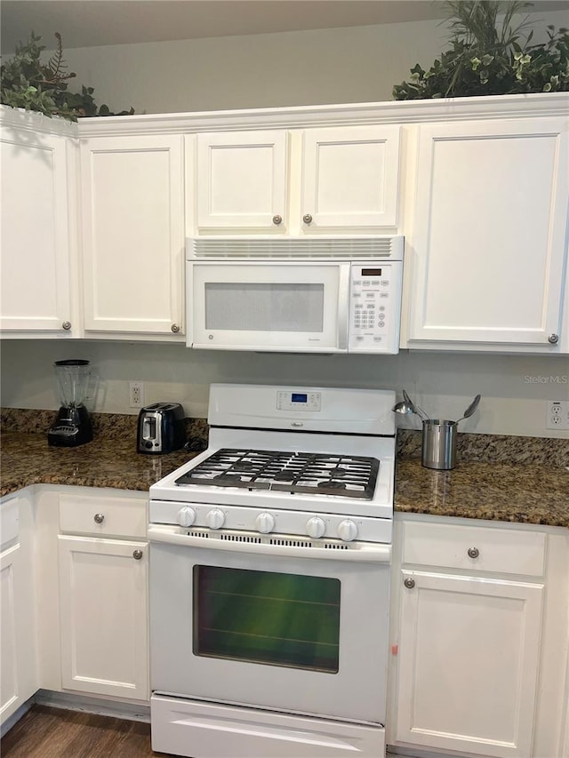 kitchen featuring dark stone counters, white appliances, and white cabinetry