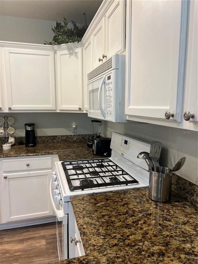 kitchen with dark stone counters, white appliances, dark hardwood / wood-style floors, and white cabinets