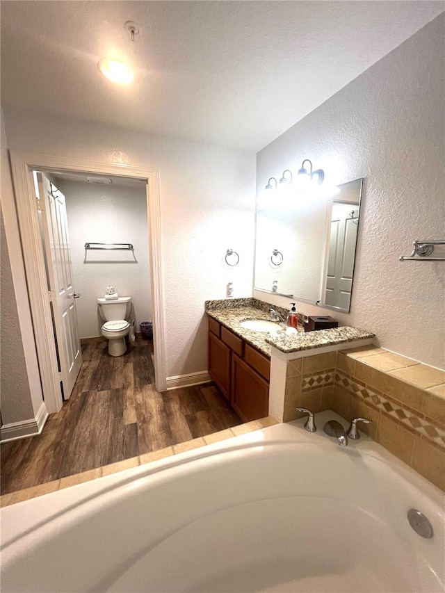 bathroom featuring vanity, a washtub, toilet, and wood-type flooring