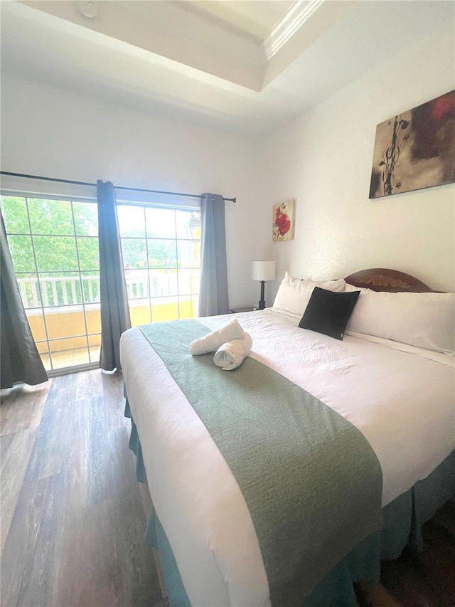 bedroom with ornamental molding, access to exterior, hardwood / wood-style flooring, and a raised ceiling